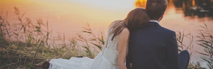 Wedded couple sitting next to water on the grass