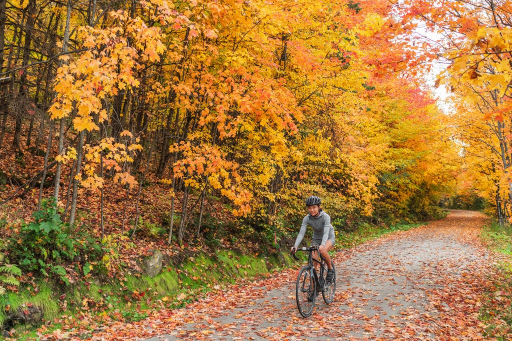 woman cycling in autumnal woods surrounded by orange leaves