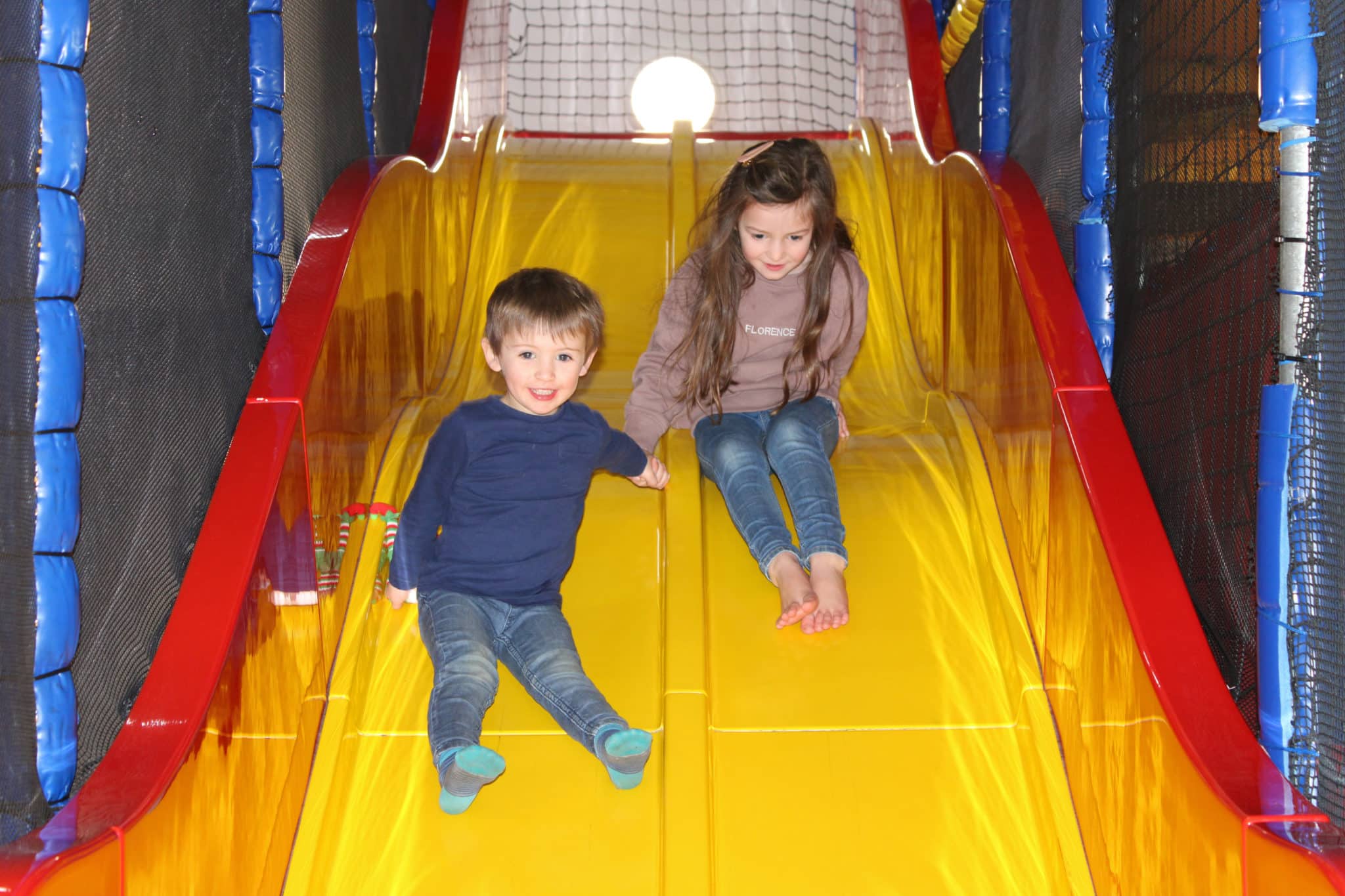 Two kids going down the slide in the soft play area