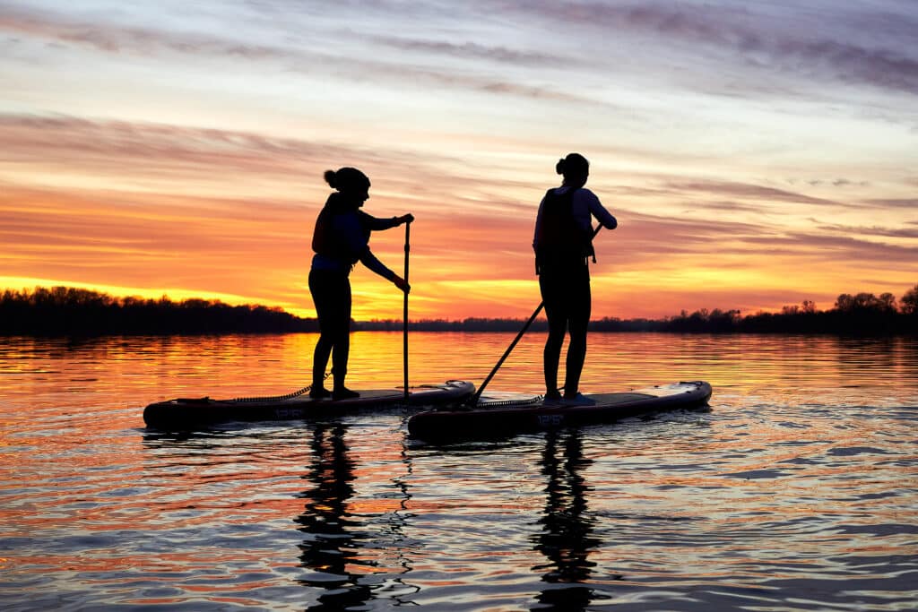Two people paddle boarding on calm water at sunset during an outdoor wellness event in Kent, part of a summer solstice weekend with nature activities and things to do this summer at Bewl Water