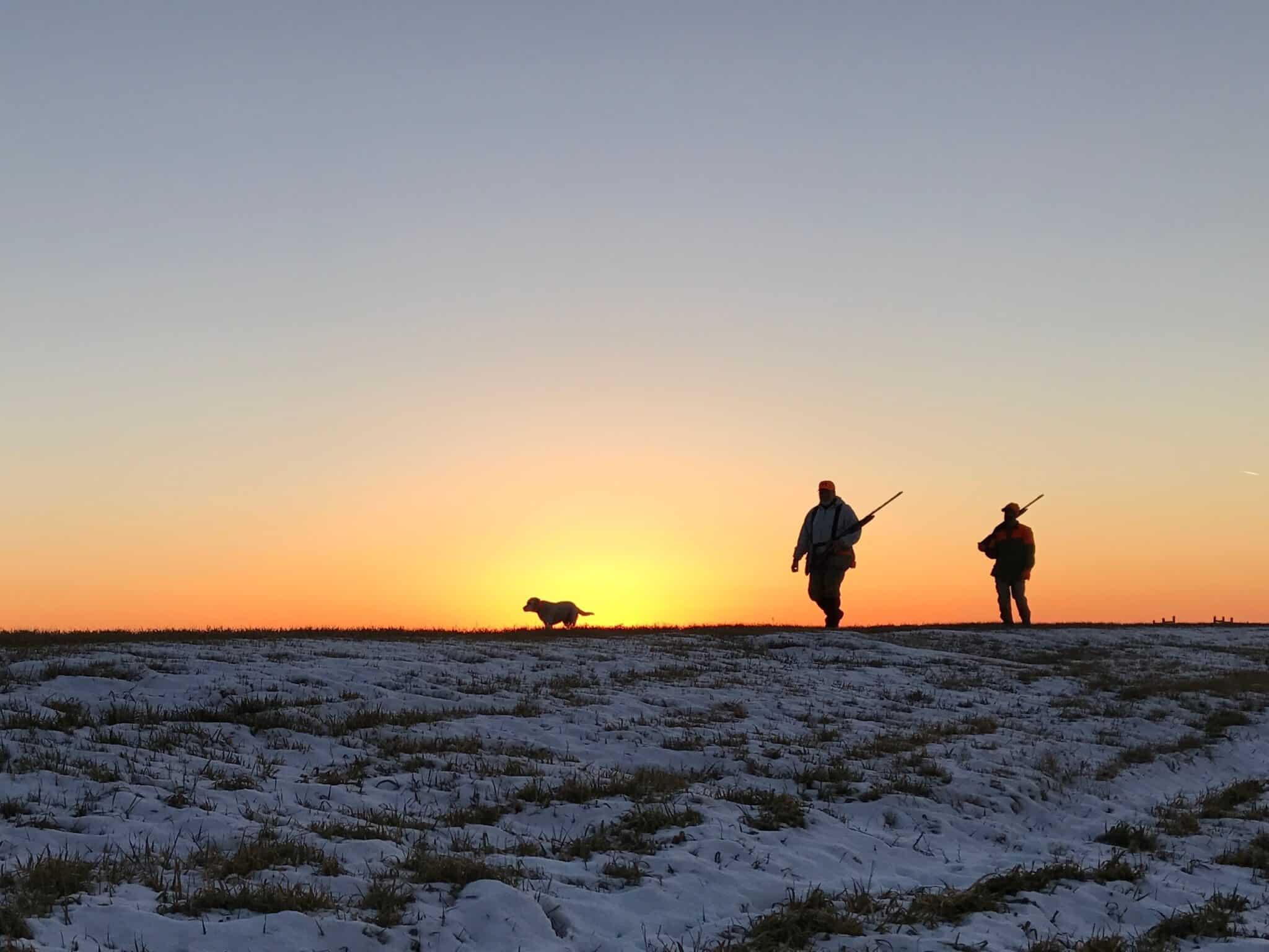Hunters,And,Dog,Silhouetted,Against,A,Winter,Sunrise,On,Snow-covered
