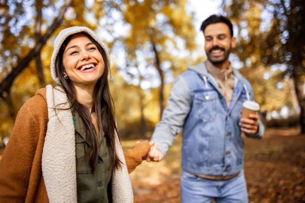 Smiling couple enjoying an autumn walk near Bewl Water, holding hands with takeaway coffee from a dog-friendly café.